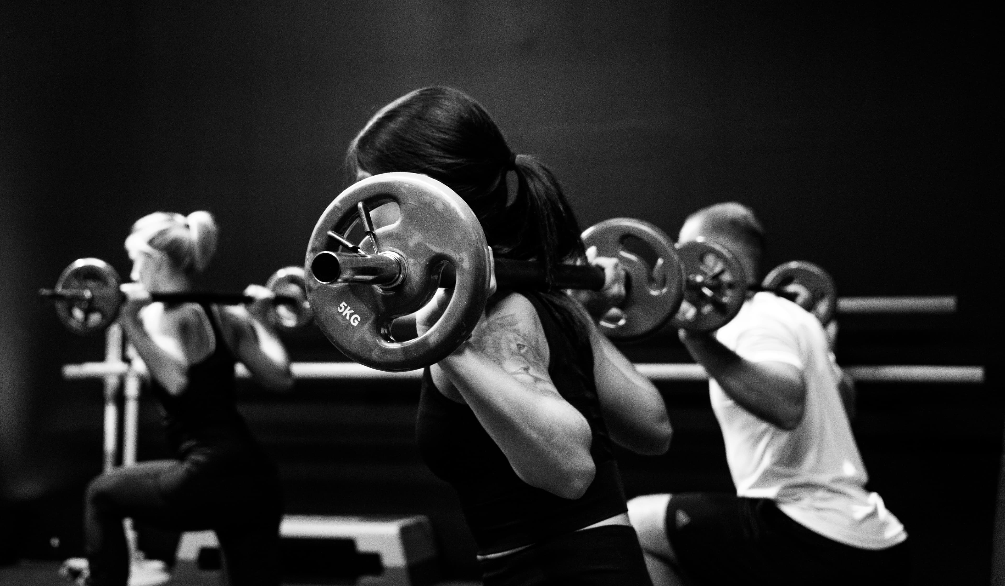 Three people lifting barbells together in a gym